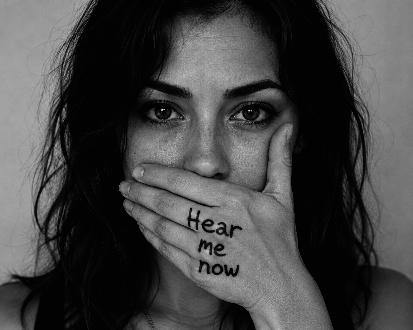A woman holding her hand over her mouth with the words 'Hear me now' written on it